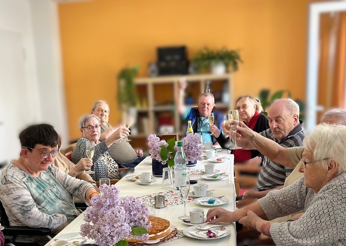Senior*innen sitzen am Kaffeetisch und stoßen mit Sekt an