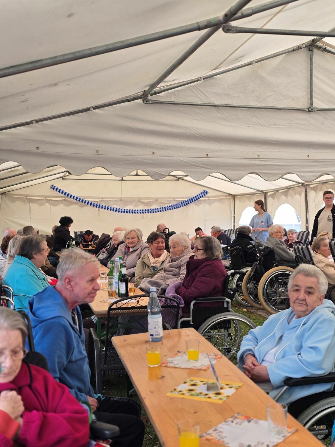 das Festzelt mit den Bewohner*innen an den Bierzeltgarnituren