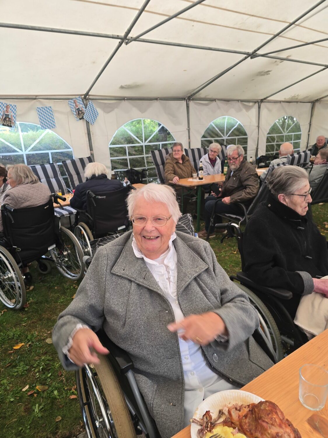 eine Bewohnerin lacht in die Kamera, daneben sieht man weitere Bewohner*innen im Festzelt