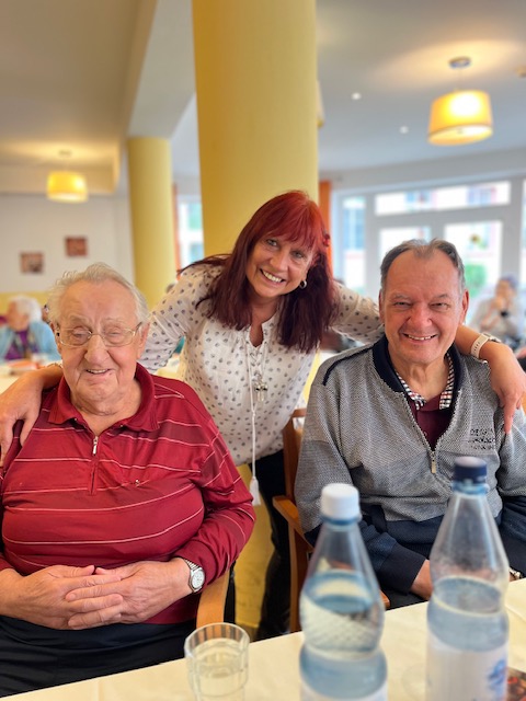 zwei Bewohner und eine Pflegerin lächeln für das Foto